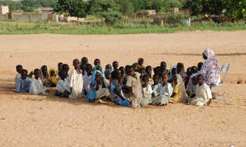 A group of children during a lesson outdoors, sat on the ground.